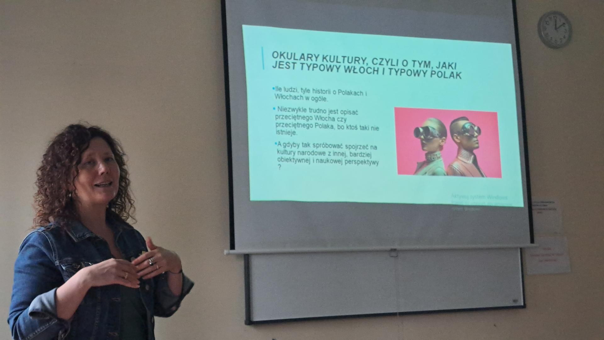 Zdjęcie przedstawia slajd z informacją, że osoba prowadząca wykład mówi o programie Erasmus+. Na slajdzie widnieje tytuł "Program Erasmus+". Osoba prowadząca wykład jest widoczna na tle slajdu.