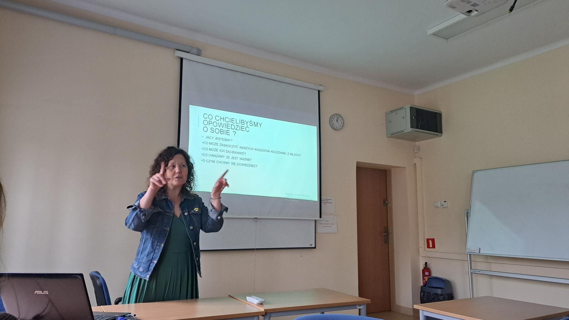 Zdjęcie przedstawia slajd z informacją, że osoba prowadząca wykład mówi o programie Erasmus+. Na slajdzie widnieje tytuł "Program Erasmus+". Osoba prowadząca wykład jest widoczna na tle slajdu.
